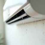 Water droplets falling from the underside of a wall-mounted split system indoor unit onto a damp, stained wall